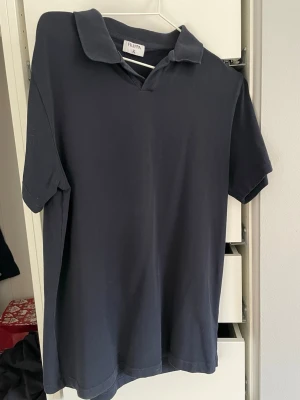 Mörkblå t-shirt från Filippa K - En stilren mörkblå piké från Filippa K med klassisk krage och korta ärmar. Tillverkad i mjuk bomull som känns skön mot huden. Perfekt för dig som gillar en clean och enkel look. Riktigt bekväm på sommaren för allt möjligt bruk.