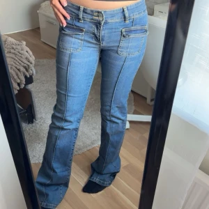 Blå bootcut jeans med fickdetaljer - Snygga helt slutsålda blå bootcut jeans med markerade sömmar framtill och stora fickor med lock. Midjemått: 36cm rakt över, Innerbenslängd: 80cm.