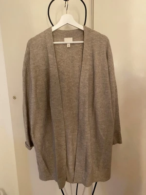 Beige oversized kofta från H&M - Mysig beige oversized kofta från H&M i mjukt stickat material. Koftan har öppen front utan knappar, långa ärmar och ribbade muddar. Perfekt att slänga över en t-shirt eller topp för en avslappnad look.
