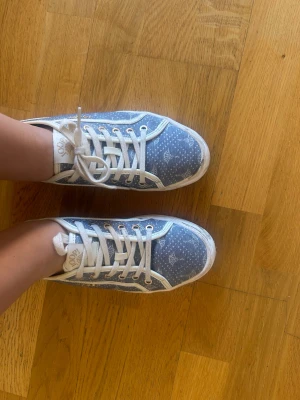 Blåa sneakers från Joop! med mönster - Snygga blåa sneakers från Joop! med vitt mönster och vita detaljer. Skorna har vita snören, vita sulor och guldfärgade öljetter. Tillverkade i tygmaterial med Joop!-logga på sidan och plösen. Perfekta för en trendig och avslappnad look.