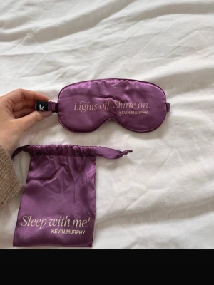 Lila sovmask i satin från Kevin Murphy - Snygg lila sovmask i glansigt satinmaterial från Kevin Murphy. Kommer med en matchande påse med texten 'Sleep with me'. Perfekt för att blockera ljus och få en bättre sömn.