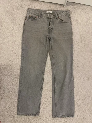 Grå raka jeans från Gina Tricot - Säljer ett par grå raka jeans från Gina Tricot med klassisk femficksmodell och knappgylf. Jeansen har en avslappnad passform och är tillverkade i slitstark denim. Perfekta för dig som gillar en enkel och stilren look.