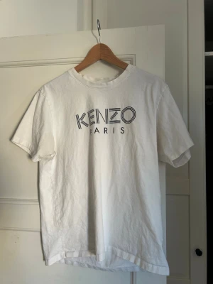 Vit Kenzo Paris t-shirt i bomull - Snygg vit t-shirt från Kenzo Paris med klassisk logga tryckt framtill. Tillverkad i mjuk bomull och har en normal passform med korta ärmar och rund hals. Perfekt för en clean och stilren look.