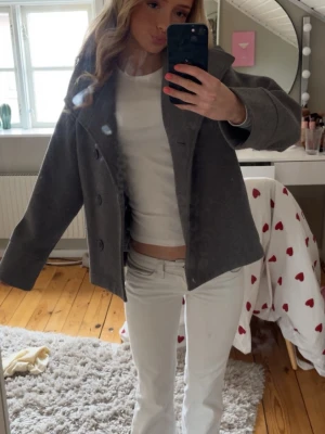 Grå ullrock  - Snygg grå rock i ullmix med bred krage och dubbelknäppning framtill. Kortare modell som ger en trendig siluett och passar perfekt till både jeans och kjol. Klassisk design utan synligt märke, enkel att matcha till olika outfits.