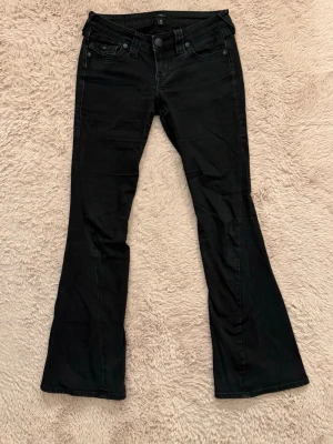 True Religion jeans - Snygga svarta bootcut jeans från True Religion med knappar på bakfickorna. Jeansen har låg midja och utsvängda ben och är i storlek W25, men passar mig som brukar ha W28. Bra sick men lite urtvättade så de har tappat den svarat färgen pyttelite. Nypris: 1200😇😇