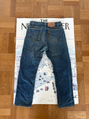 Levi's 505 raka blå jeans - Säljer ett par klassiska Levi's 505 jeans i blå denim med raka ben och normal midja. Jeansen har två bakfickor, orange Levi's-tagg och läderpatch bak i midjan. Perfekta för en avslappnad och tidlös stil. Materialet är 100% bomull. Troligen från 1969