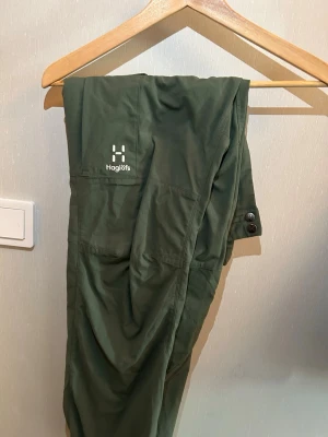 Gröna vandringsbyxor från Haglöfs. Använt 1 gång. Stolek 50/ M - Snygga mörkgröna cargobyxor från Haglöfs med flera praktiska fickor och knappdetaljer. Tillverkade i ett lätt och slitstarkt material som passar perfekt för utomhusaktiviteter. Klassisk passform och diskret logga på benet.