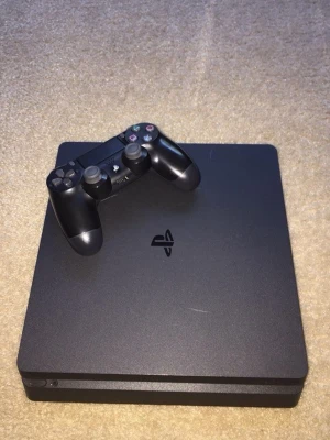 PlayStation 4 Slim med handkontroll - Säljer en svart PlayStation 4 Slim från Sony med tillhörande svart DualShock 4-handkontroll. Konsolen har en stilren, fyrkantig design med rundade hörn och mattsvart finish. Perfekt för gaming och streaming.kapel va trasig men har fixat ny kapel så den funkar hur bra som helst plus du får med typ 10+spel 