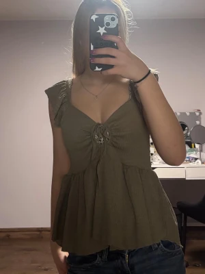  ribbad blus med volang - Brun blus från lager 157 i ribbad bomullsblandning. Modellen har volangdetaljer vid axlarna, knyt framtill och lätt v-ringad hals. Passformen är loose och toppen är ärmlös, perfekt för sommarens alla looks.