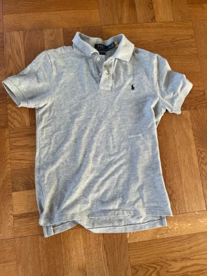 Ralph Lauren piké - Snygg och fräsch grå Ralph Lauren piké i slim fit med Ralph Lauren märket broderat i blått. Barnstorlek som passar xs i herrstorlek. Inga defekter alls
