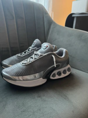 Nike dn silvergrå sneakers size 38 - Nike dn  sneakers i silvergrå mesh och syntetmaterial med ikoniska fjädrande Shox-dämpning i hälen. Skorna har vita och svarta detaljer, samt en futuristisk design med rundad tå och snörning. Perfekta för dig som gillar sportig och modern stil. Inga hål osv endast en liten röd fläck men syns knappt.