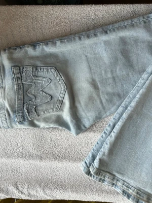 Ljusblå bootcut jeans från Gina tricot  - Säljer ett par ljusblå bootcut jeans från Gina tricot med W-broderade bakfickor. Jeansen har låg midja och utsvängda ben. Tillverkade i klassisk denim med snygg tvätt och detaljerade sömmar.