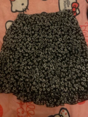 Svart blommig kjol från Amisu - Kort svart kjol från Amisu med vitt blommönster. Kjolen har en lätt utställd form och resår i midjan för skön passform. Perfekt för dig som gillar en söt och trendig stil. Materialet känns mjukt och följsamt.