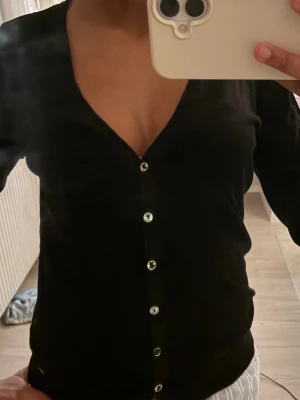 Elena Gilbert\bella swan 🦢 tröja - Stilren svart kofta med v-ringning och silvriga knappar hela vägen framtill. Långärmad modell i mjukt och tunt material som passar perfekt till lager på lager. Enkel att matcha med olika outfits.