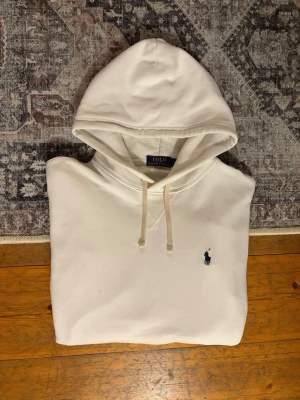 Vit Ralph Lauren Hoodie - Hej!👋  Säljer en vit Ralph Lauren Hoodie mer den broderade mörkblå pony-loggan på bröstet. Hoodien är I mycket fint skick, men är lite nopprig på botten. Absolut inget som man tänker på vid användning. Storlek M. Hör av er vid frågor!💯