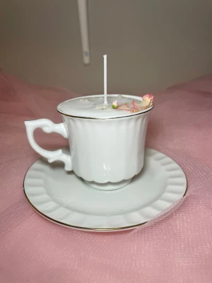 Doftljus i vaniljdoft i en vit tekopp med fat - Det här ljuset är gjort av återanvändbara material. Tekoppen är köpt secondhand och stearinet är från kyrkor som tänkte slänga det. Det här ljuset har en svag doft utav vanilj, så känsliga även kan använda det. Det här ljuset har även torkade blommor på som dekoration. 