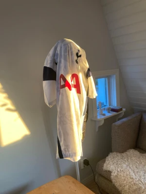 Tottenham Hotspur matchtröja vit - Säljer en vit Tottenham Hotspur matchtröja från Nike med mörkblå detaljer och grafiskt mönster. Tröjan har klubbens emblem på bröstet och röd AIA-logga på framsidan. Tillverkad i lätt och ventilerande funktionsmaterial, perfekt för fotboll.