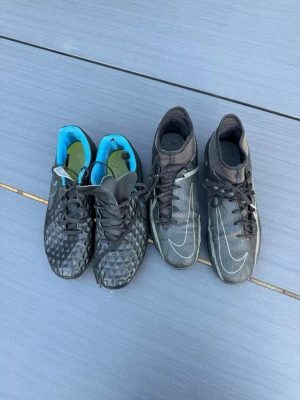Nike Phantom GT fotbollsskor svart - Säljer två par Nike Phantom GT fotbollsskor i svart med vita detaljer. Ena paret har blå insida och strukturmönster på ovandelen, det andra paret har högre skaft och tydliga vita linjer. Båda paren har snörning och är tillverkade i syntetmaterial för bra bollkontroll. Dem blåa skorna är st 39,5 och de svarta är 40