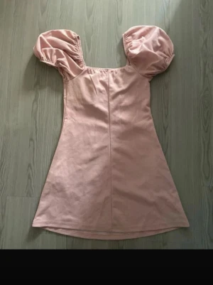 Rosa kort klänning med puffärmar - Supersöt rosa kort klänning med stora puffärmar och fyrkantig urringning. Klänningen har en enkel, rak passform och är perfekt för dig som gillar en romantisk och trendig stil. Tillverkad i mjukt tyg som känns skönt mot huden.
