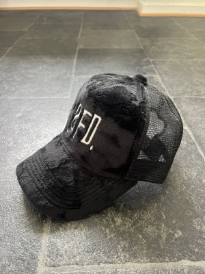 SampeV2 collab keps från Classified  - Snygg svart keps från CLFD med broderad vit logga framtill. Framsidan är i mjuk fuskpäls och baksidan har meshpanel för extra ventilation. Justerbar passform med klassisk böjd skärm. Perfekt för en trendig streetwear-look. Collab med SampeV2 , justerbar storlek (one size) 