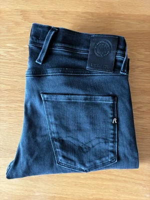 Svarta jeans från Replay - Snygga mörkblå jeans från Replay med klassisk femficksdesign och smal passform. Jeansen har en diskret logga på bakfickan och läderpatch med Replay-märke i midjan. Perfekta för en trendig och avslappnad look.