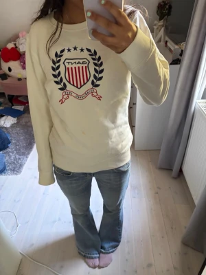 Vit sweatshirt från Gant med tryck - Vit sweatshirt från Gant med stort tryck framtill i rött, blått och svart. Tröjan har rund halsringning och långa ärmar. Klassisk och stilren design med collegekänsla, perfekt till jeans eller kjol. Den har några fläckar som jag inte vet ifall det går bort i tvätten! Sitter som en xs.