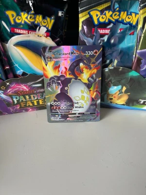 Charizard VMAX Pokémonkort - Säljer ett Charizard VMAX Pokémonkort med färgstark och glansig design. Kortet har motiv av Charizard i svart och orange med eldflammor och holografiska detaljer. Perfekt för samlare eller Pokémon-fans som vill utöka sin kortsamling.tar även emot trades