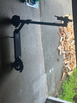 Svart elscooter med laddare och lås - Säljer en svart elscooter med tillhörande laddare och ett grönt cykellås. Scootern har stora hjul och en räfflad ståplatta för bra grepp. Perfekt för att ta sig runt i stan på ett smidigt sätt.