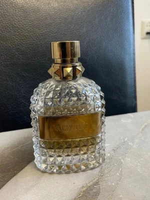 Valentino parfym 100 ml - Snygg parfym från Valentino i en lyxig, transparent glasflaska med nitar och gulddetaljer. Flaskan rymmer 100 ml och har en exklusiv känsla med sitt mönstrade glas och guldiga etikett. Perfekt för dig som gillar stilrena och eleganta dofter.