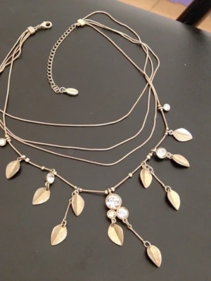 Guldigt halsband med löv och kristall stenar - Snyggt halsband i guldton med flera tunna kedjor och hängande lövformade berlocker samt glittrande kristall stenar. Perfekt accessoar för att lyfta din outfit med en bohemisk touch. Justerbar längd med kedja och karbinlås. HALSBANDET ÄR VINTAGE OCH GÅR EJ ATT FÅ TAG PÅ JUST DENNA DESIGNEN NÅGONSTANS! 
