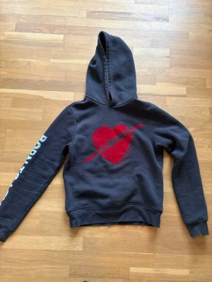 Svart hoodie Scotch & Soda Born To Love - Svart hoodie från Scotch & Soda med stor röd hjärtgrafik och texten 'Born To Love' på bröstet. Tryck på ena ärmen. Klassisk huva och ribbade muddar. Perfekt för dig som vill sticka ut med en cool streetstyle-look.