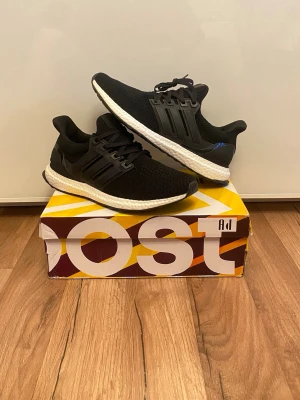 Adidas Ultra Boost storlek 45 - Svarta Adidas Ultra Boost sneakers med stickad ovandel och vita Boost-sulor. Skorna har klassisk låg profil, svarta plastdetaljer vid snörningen och diskret branding på plösen. Perfekta för dig som gillar stilrena och bekväma sneakers. Kan även passa 43-44. Helt sprillans nya, aldrig använda, säljer för dem inte passar.
