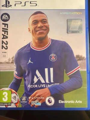 FIFA 22 till PS5 - FIFA 22 till PlayStation 5 med HyperMotion-teknologi. Spelet har en blå plastfodral, med omslag som visar en fotbollsspelare i PSG-tröja. Inuti finns både skiva och manual. Perfekt för dig som älskar fotboll och vill spela de största ligorna.