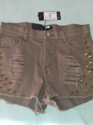 Bik Bok ,,slitna,, shorts med nitar Nya stl M New Look - Snygga shorts från Bik Bok med slitna detaljer och råa kanter. Utsmyckade med guldiga nitar på sidorna för en edgy look. Klassisk femficksmodell och knappstängning framtill. Perfekta för sommaren!Helt nya med tagsen kvar! 