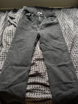 Mörk Gråa raka jeans med fem fickor - Snygga grå jeans med rak passform och klassisk femficksdesign. Jeansen har bälteshällor och silverfärgade nitar vid fickorna. Perfekta för en avslappnad och stilren look. Materialet är denim i bomull.