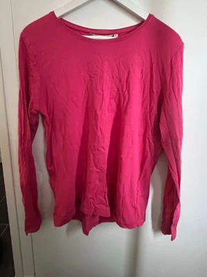 Rosa långärmad topp  - En enkel och stilren rosa långärmad topp med rund halsringning. Tillverkad i mjuk bomull som känns skön mot huden. Perfekt att matcha med jeans eller kjol för en avslappnad look.