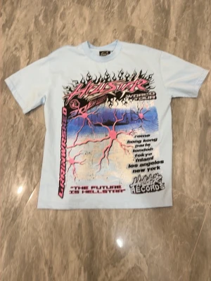 Ljusblå grafisk t-shirt från Hellstar - Cool ljusblå t-shirt från Hellstar med stort grafiskt tryck i rosa, svart och blått framtill. T-shirten har klassisk passform, rund hals och korta ärmar. Perfekt för dig som gillar streetwear och unika prints.