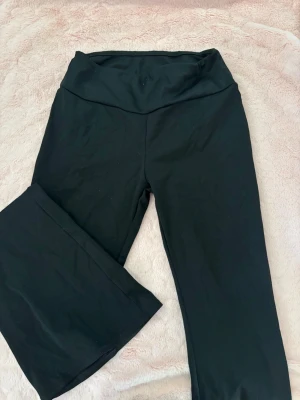 Svarta leggings med fickor och knappar - Svarta leggings med två bakfickor med lock och stora knappar. Materialet är stretchigt och mjukt, perfekt för en avslappnad stil. Snygg rynkdetalj bak ger extra form. Passar dig som gillar bekväma och trendiga byxor.