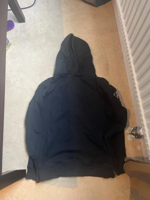 Svart hoodie från Calvin Klein Jeans - Snygg svart hoodie från Calvin Klein Jeans med klassisk huva och magficka. Perfekt för en avslappnad och cool stil. Diskret logga på ärmen och mjukt material som känns skönt mot huden. Passar både XS och XSS