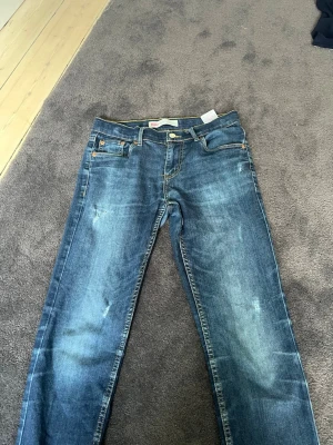 Blå raka jeans med slitningar - Snygga blå jeans med raka ben och diskreta slitningar framtill. Klassisk femficksmodell med kontrastsömmar och normalhög midja. Perfekta för en avslappnad stil och passar till det mesta.