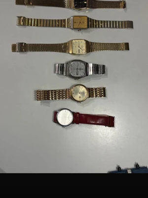 Mix av vintage armbandsur i metall - Säljer ett gäng klassiska armbandsur i olika stilar och färger. Här finns både guld- och silverfärgade klockor med metallarmband samt en stilren klocka med rött läderband. Flera av klockorna har fyrkantiga urtavlor och retrovibbar. The watches is reparation object the do not work 