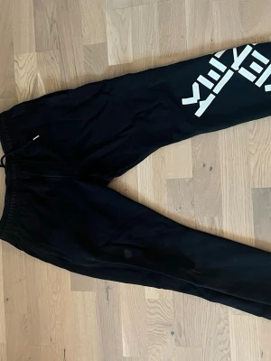 Svarta Kenzo mjukisbyxor med tryck - Svarta mjukisbyxor från Kenzo med stort vitt logotryck på ena benet. Byxorna har resår och dragsko i midjan för skön passform. Perfekta för en chill och avslappnad stil. Tillverkade i mjukt material som känns nice mot huden.