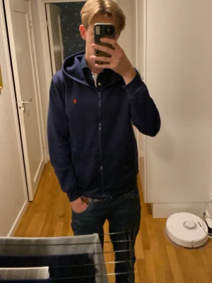 Mörkblå hoodie från Polo Ralph Lauren - Mörkblå hoodie med dragkedja från Polo Ralph Lauren. Klassisk design med huva och fickor framtill. Liten röd logga broderad på bröstet. Fet för sommar outfits🔥