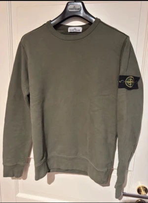 Stone Island grön sweatshirt - Snygg grön sweatshirt från Stone Island med klassisk patch på vänster ärm. Tröjan har rund halsringning, ribbade muddar och är tillverkad i mjuk bomull. Perfekt för en avslappnad streetwear-look.
