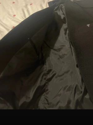Svart kavaj med ståkrage - Snygg svart kavaj med modern ståkrage och diskret struktur i tyget. Kavajen har en bröstficka och är helfodrad på insidan. Perfekt för dig som vill ha en stilren och trendig look. Materialet känns mjukt och följsamt.
