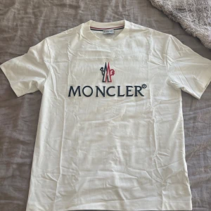 Vit Moncler t-shirt  - Snygg vit t-shirt från Moncler med stor broderad logga på bröstet i blått och rött. Tror inte den är äkta. Aldrig använd 