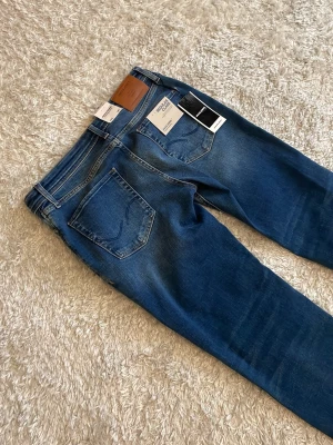 Blå jeans från Jack and Jones  - Snygga blå jeans från Jack and Jones med klassisk femficksdesign och skön passform. Jeansen har en lätt tvättad look och är tillverkade i bomull med stretch för extra komfort. Perfekta till din vardagsstil.