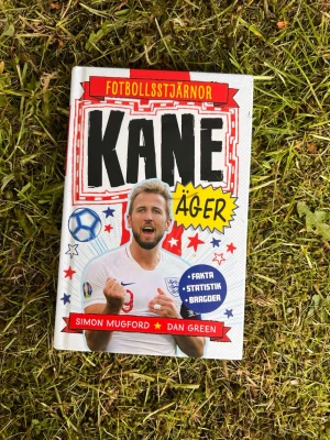 Kane äger - Fotbollsstjärnor - En färgglad och inspirerande bok om fotbollsstjärnan Harry Kane, fylld med fakta, statistik och bragder. Perfekt för dig som älskar fotboll och vill veta mer om en av Englands största spelare. Omslaget är vitt med röda, blå och gula detaljer.