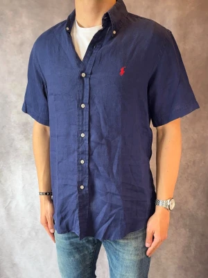 Marinblå kortärmad Ralph Lauren Linneskjorta- Stl M, Custom Fit - Riktig snygg kortärmad Ralph Lauren Linneskjorta, perfekt till sommaren! 🏖️🌊 | Mycket bra skick: 9,4/10, utan defekter  | Stl: M |  Modellen är 177cm och väger 74kg | Billigare pris vid köp av bundle 😉Hör av dig vid frågor // Galgen 🫡 