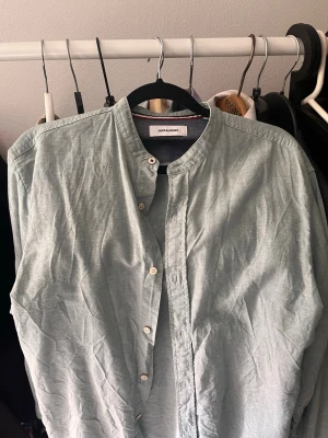 Ljusgrön skjorta från Jack & Jones - Säljer en ljusgrön skjorta från Jack & Jones med ståkrage och knappar framtill. Skjortan är i bomull och har en enkel, stilren design utan mönster. Perfekt för dig som gillar en clean look.